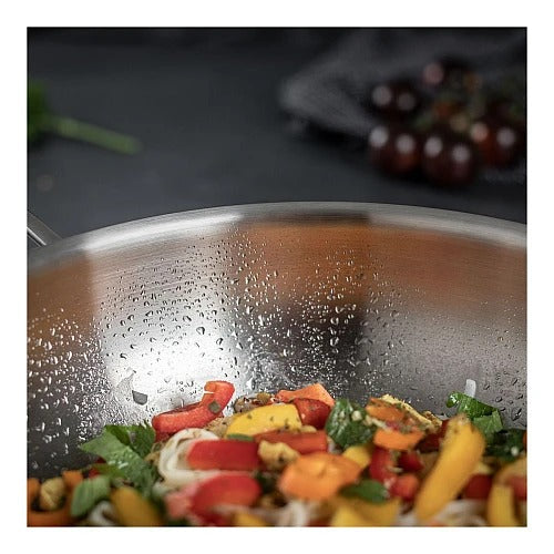 Close-up in de Culinary 5-Ply wok met deksel 28 cm gevuld met een roerbakgerecht van noedels, paprika en basilicum, met waterdruppels op de binnenwand.