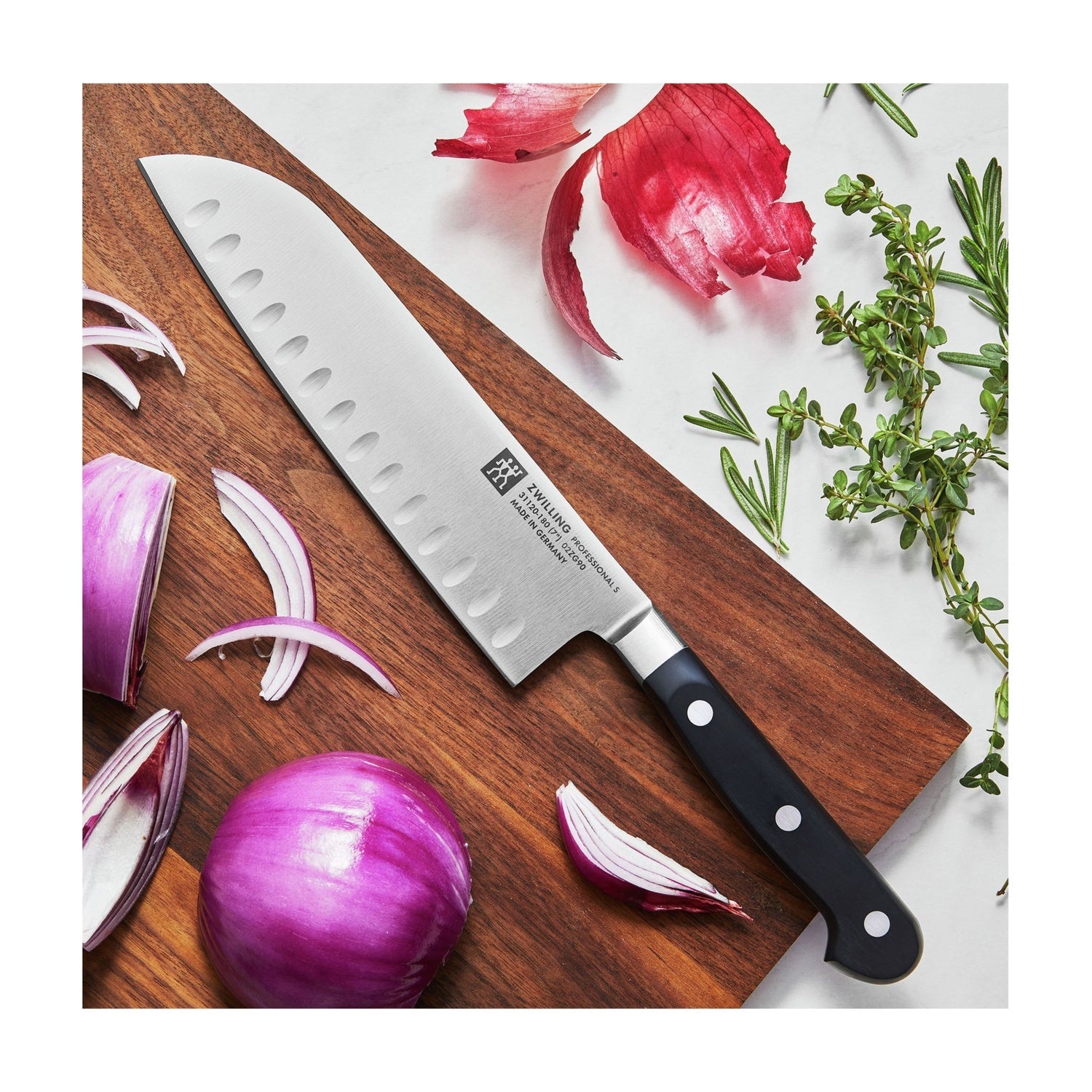 Zwilling Professional S Santokumes op een houten snijplank tussen rode ui en kruiden