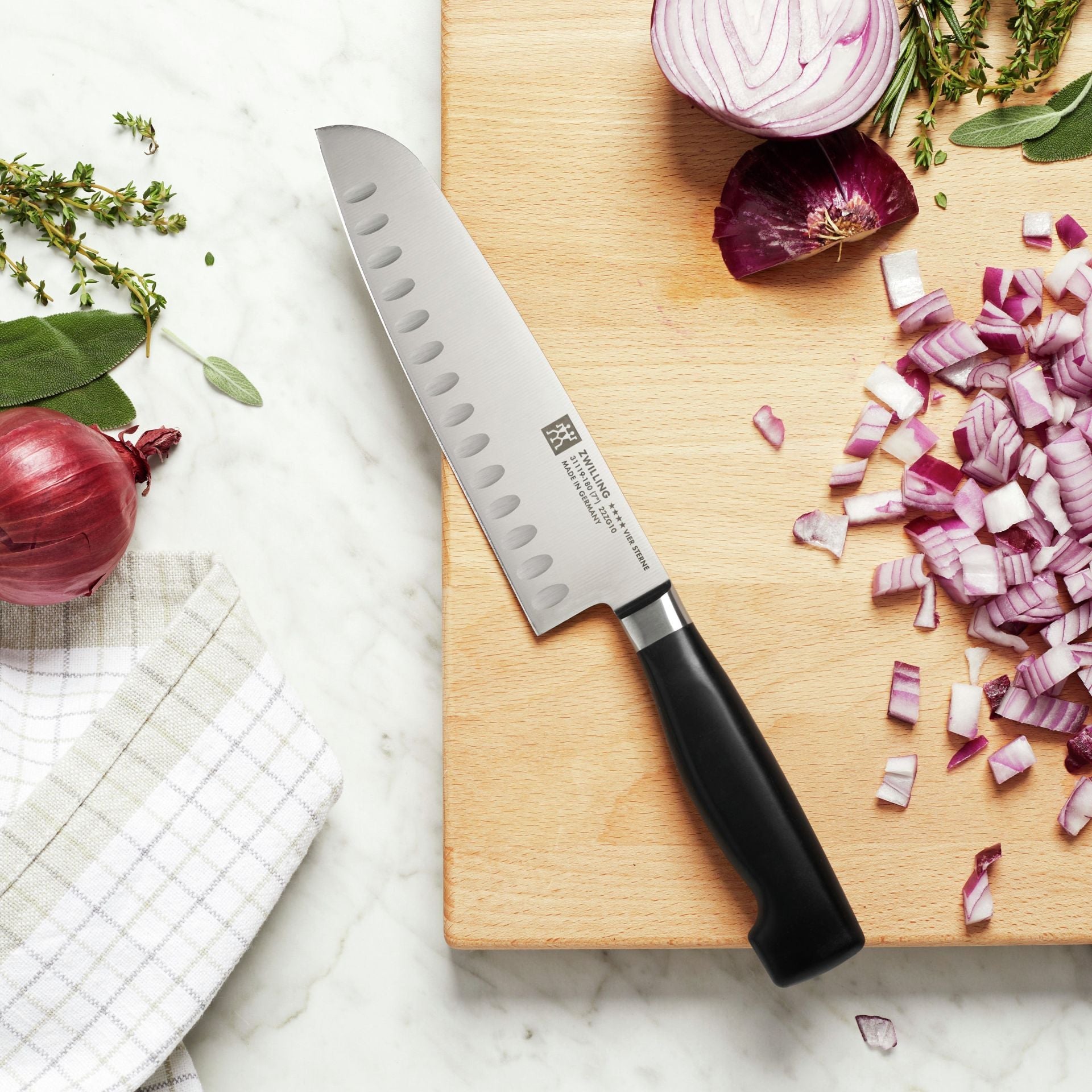 Zwilling Four Star Santokumes op een houten snijplank met rode ui en kruiden