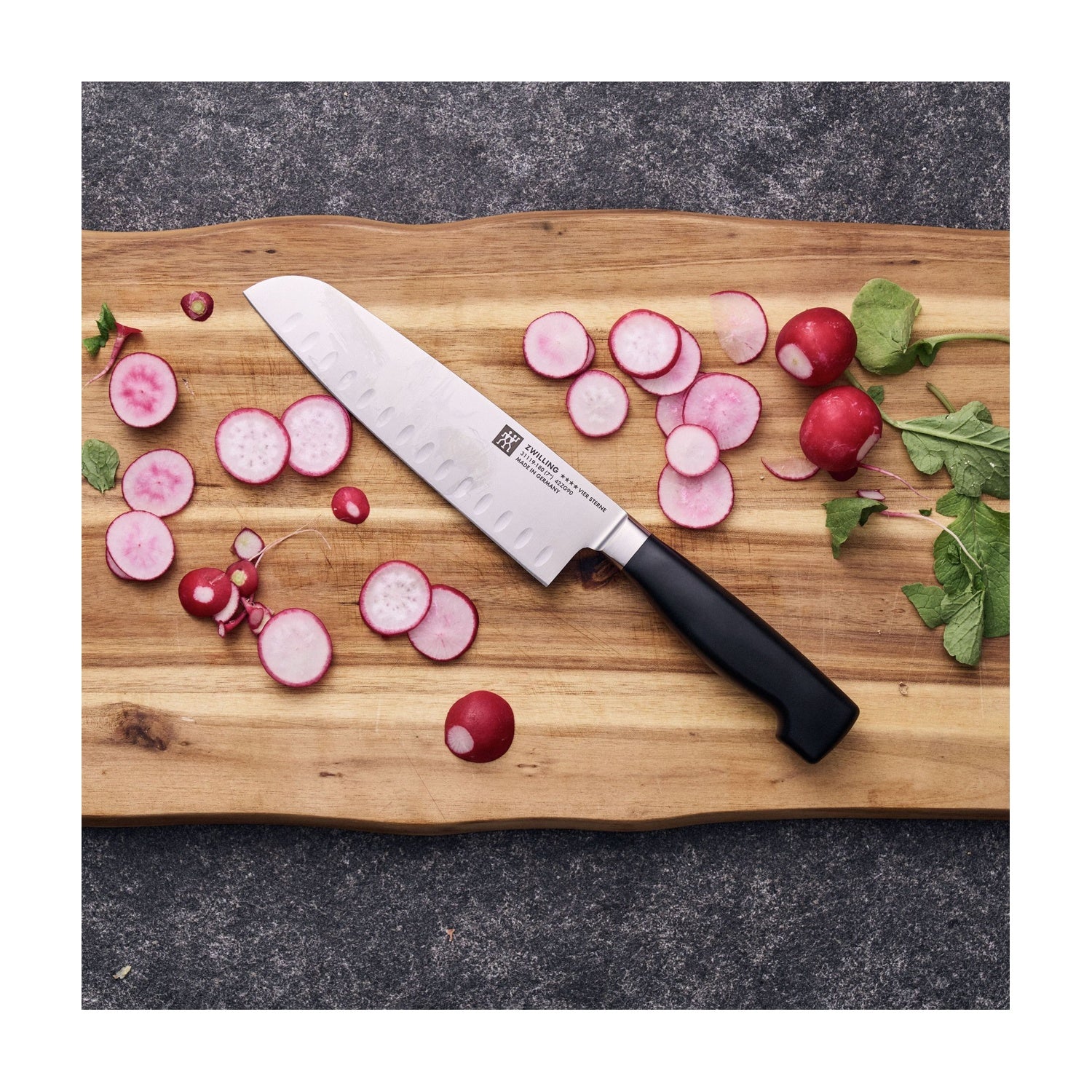 Zwilling Four Star Santokumes op een houten snijplank tussen radijsjes