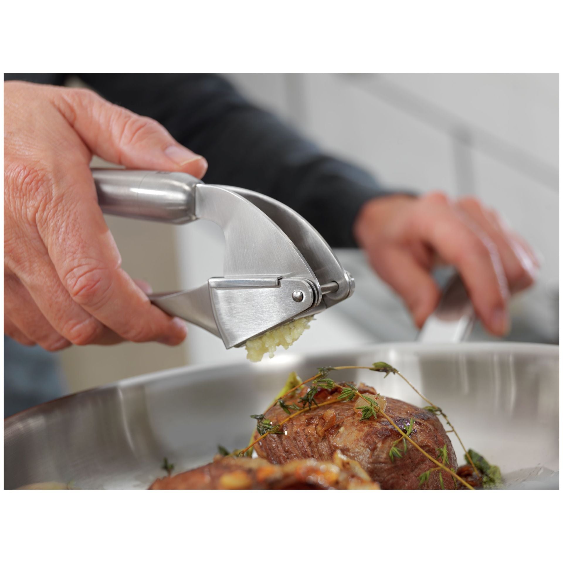 Hand knijpt met de Zwilling Pro Knoflookpers een teentje knoflook boven een gerecht