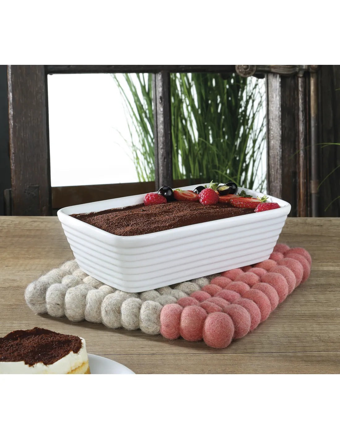 Witte ribbelschaal met tiramisu en verse bessen op een beige en koraalroze vilten onderzetter, op een houten tafel