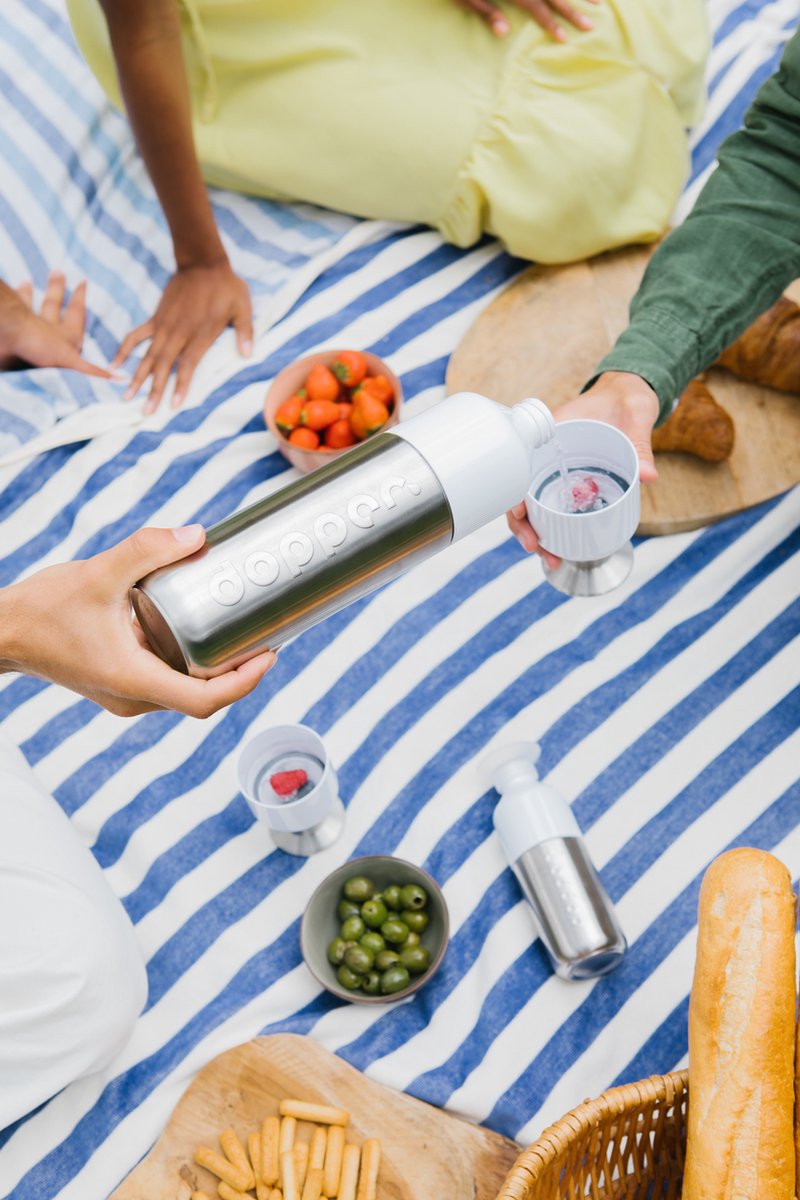Iemand schenkt water uit de Dopper Steel - 1,1 liter in een bekertje tijdens een picknick met aardbeien en olijven