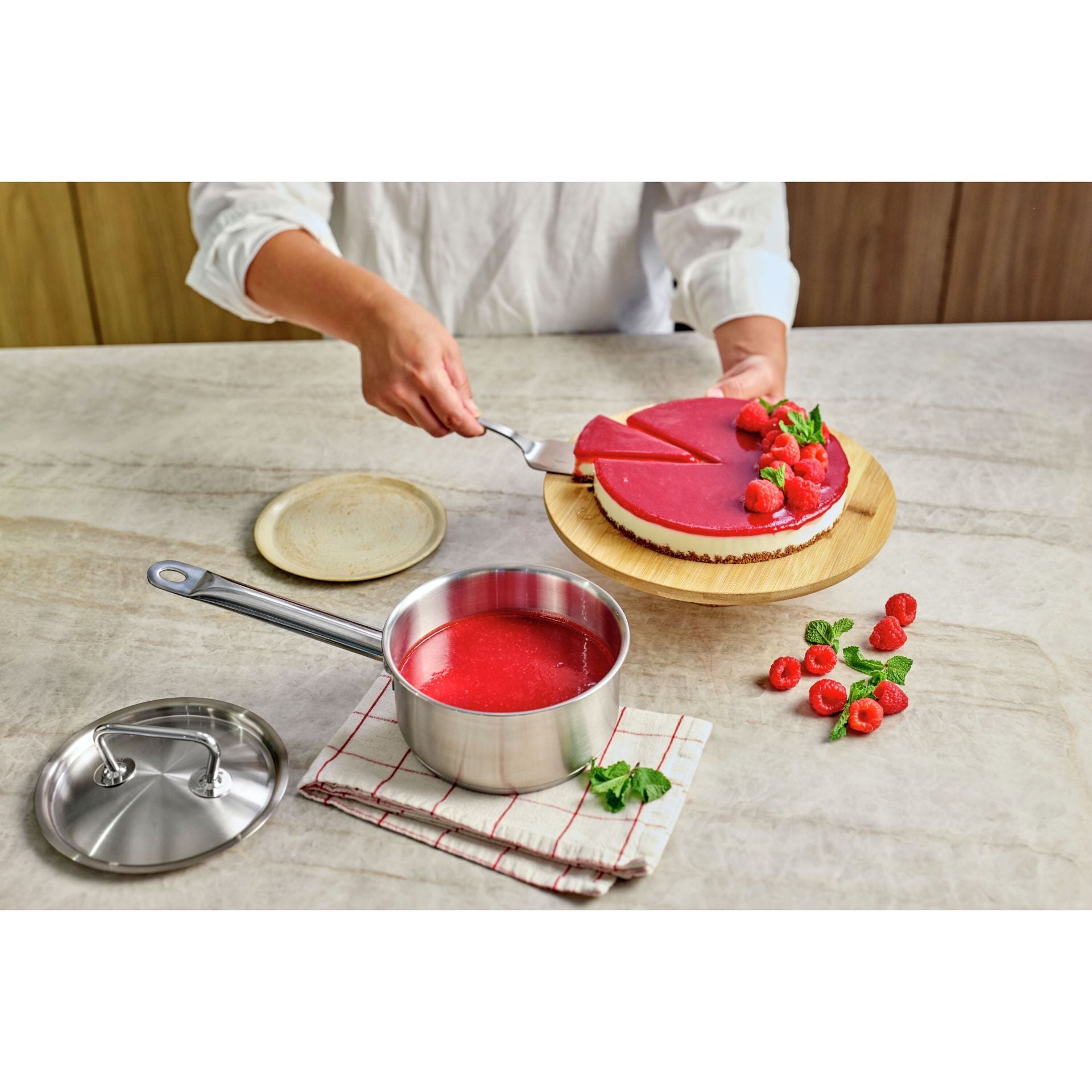 Rode vruchtenglazuur wordt bereid in de Demeyere Classic Pro 3 Steelpan 16 cm naast een taart met aardbeien