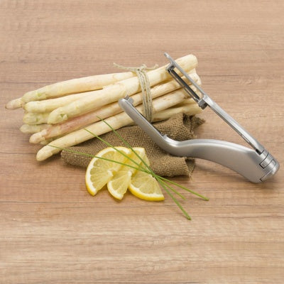 Westmark Peel-Star Alu Dubbele Aspergeschiller, zilver, naast een bosje witte asperges met citroenschijfjes
