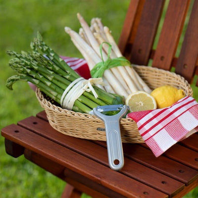 Westmark Quick Groente- en Aspergeschiller, zilver, schiller op een houten tuinstoel naast een mand asperges en citroen