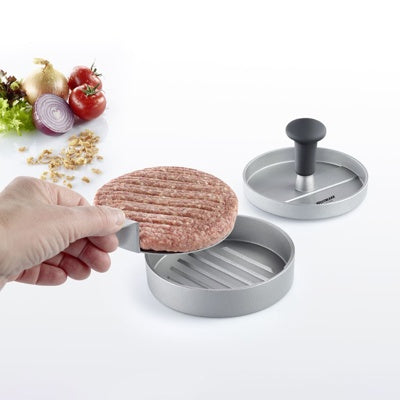 Westmark Uno Plus Hamburgerpers, aluminiumkleurig met zwarte knop, in gebruik met een hand die de geperste burger uit de vorm haalt