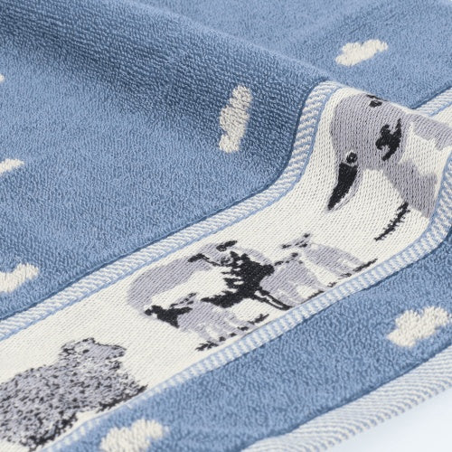 Bunzlau Castle Keukendoek - Schaap Grijs/Blauw, twee handen houden de doek naast een doek met bloemenprint ter vergelijking
