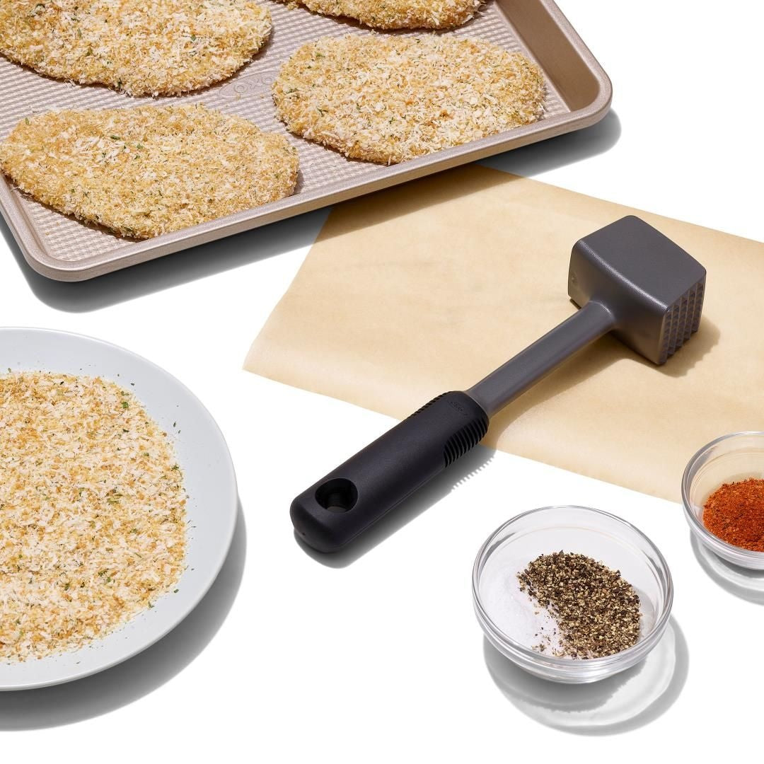OXO Good Grips Vleeshamer Kunststof in gebruik, naast bord paneermeel en schaaltjes kruiden voor het pletten van vlees