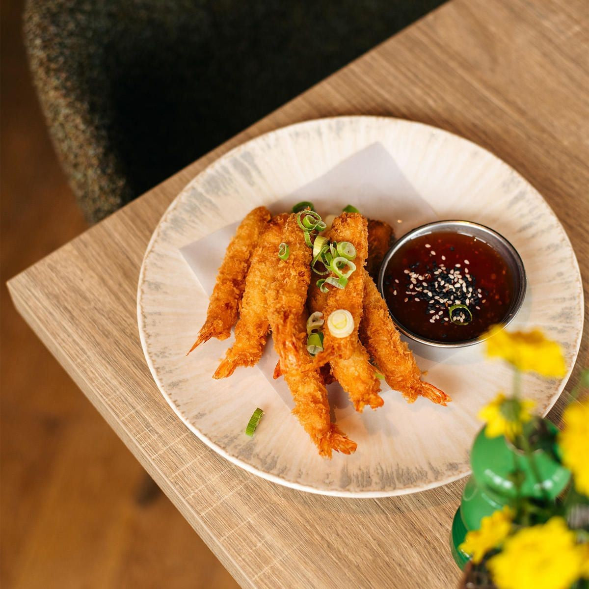 Bovenaanzicht van het bord met gepaneerde garnalen, een bakje zoete chilisaus met sesam en bosui op bakpapier