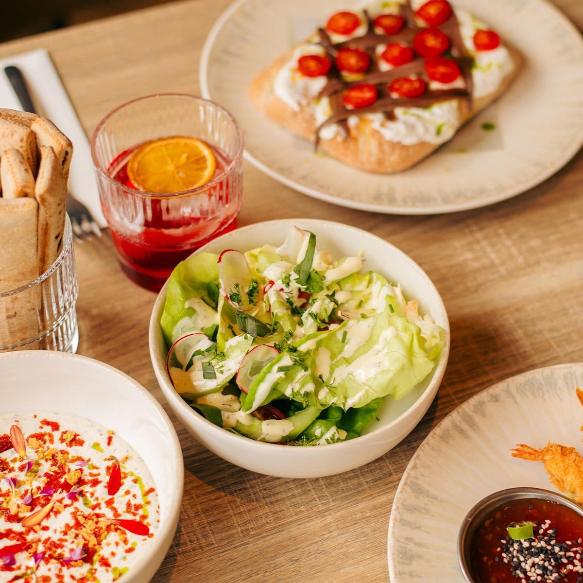 Kom met groene salade, radijs en dressing naast een glas met rode drank op een houten tafel