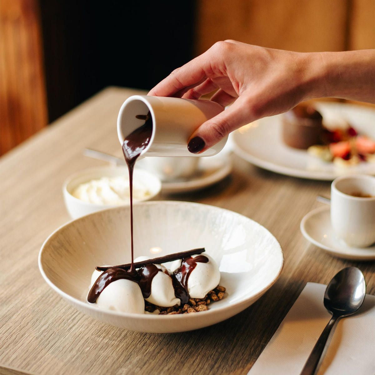 Hand giet warme chocoladesaus uit een klein kannetje op bolletjes ijs in de brede kom