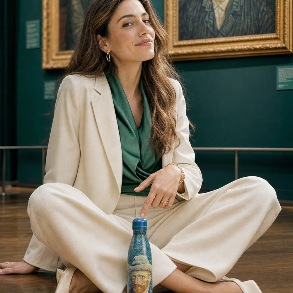 Vrouw zit kleermakerszit in een museumzaal en houdt de IZY Thermosfles Zelfportret Van Gogh tussen haar voeten