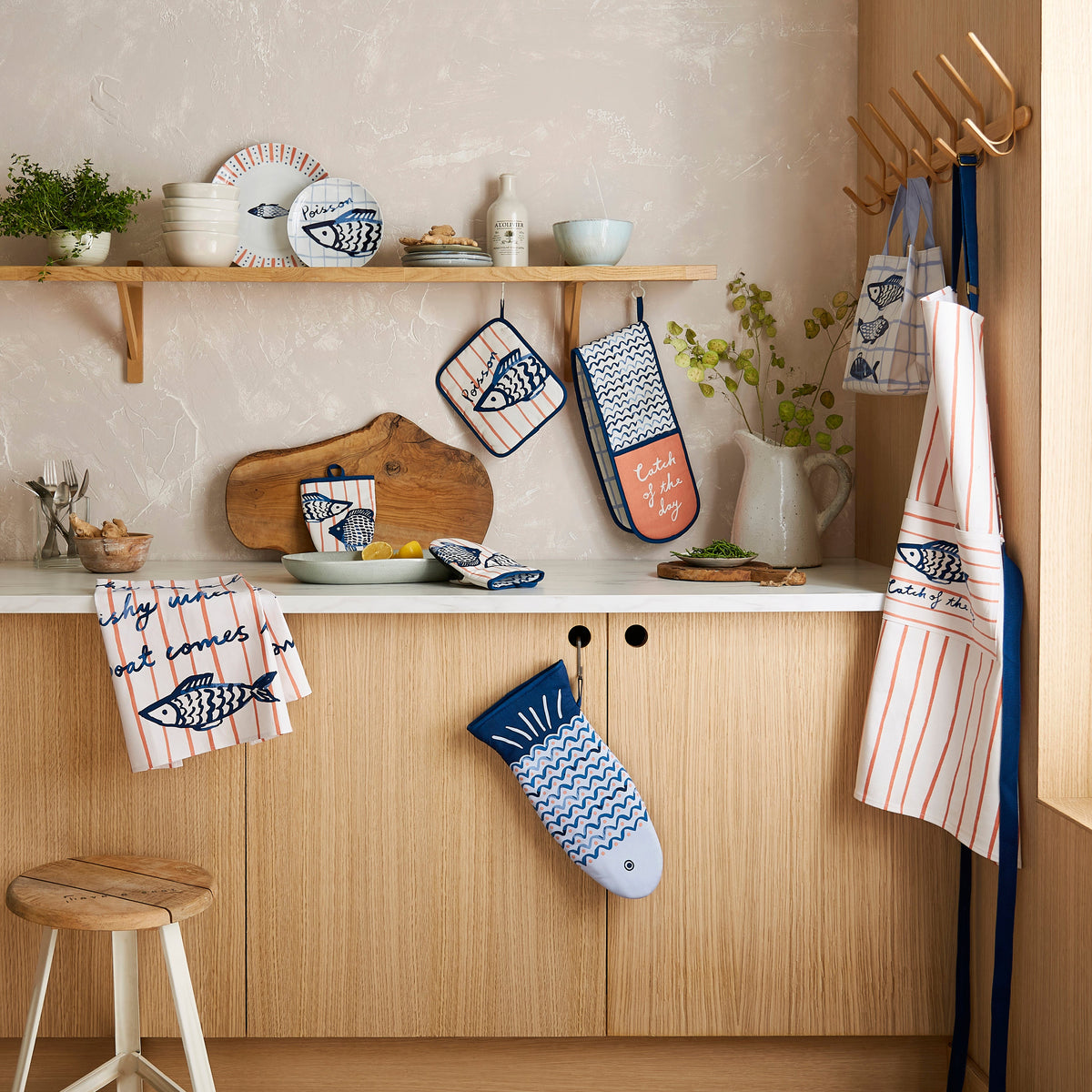 Ulster Weavers Keukenschort Katoen - Catch of the Day, schort, theedoek en pannenlap op een plank in de keuken