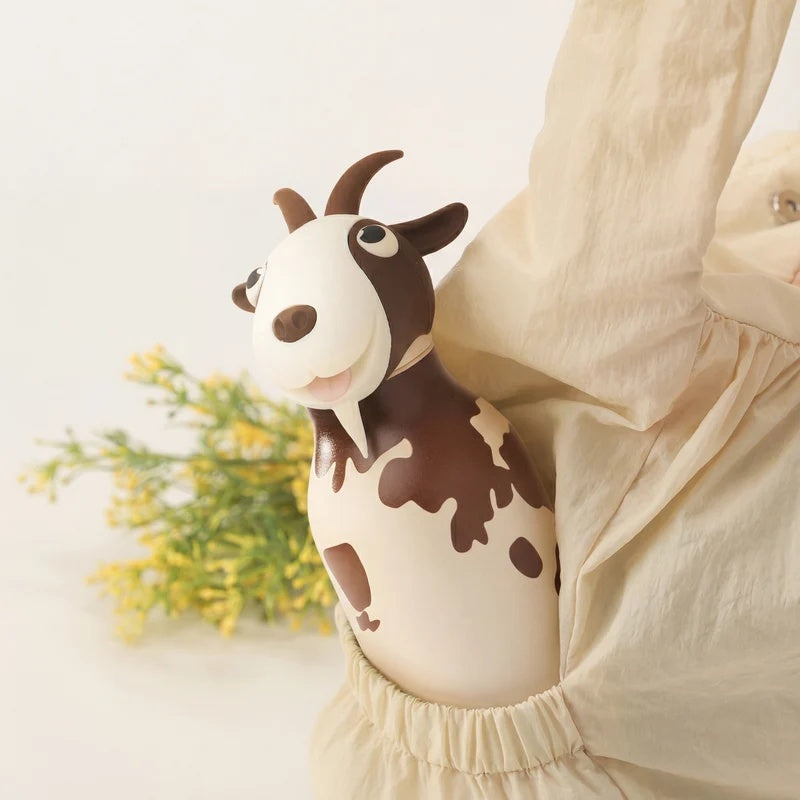 Persoon draagt de Asobu Bestie Thermosfles Geit in een zak, met bloemen op de achtergrond