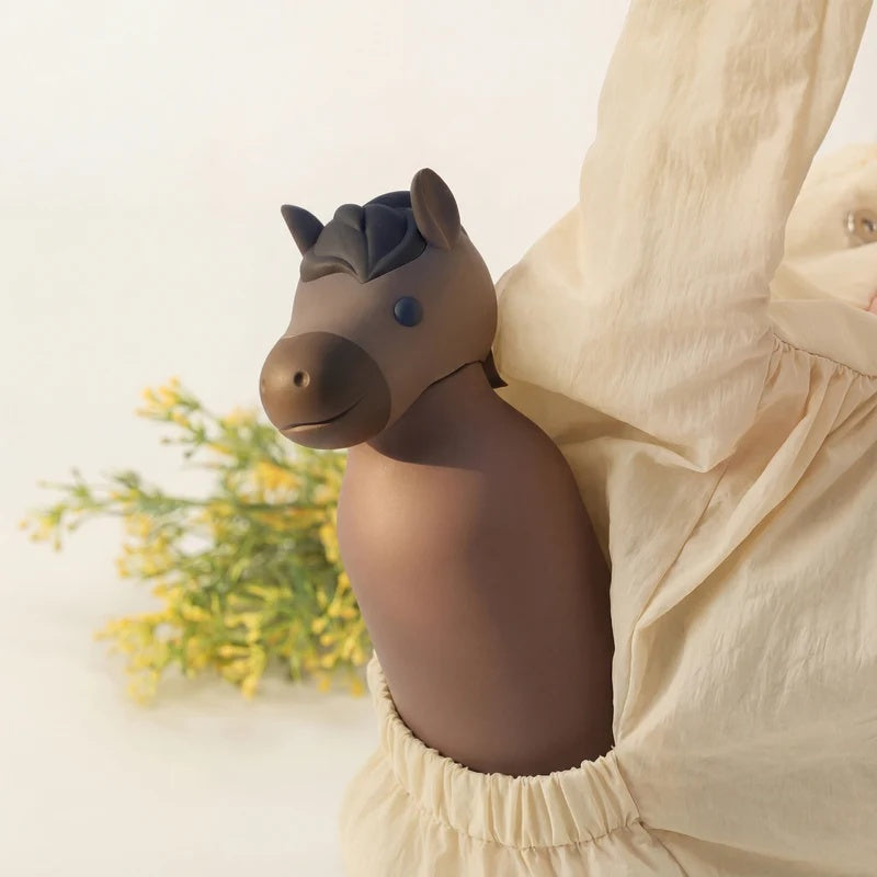 Persoon draagt de Asobu Bestie Thermosfles Paard in een zak, met bloemen op de achtergrond