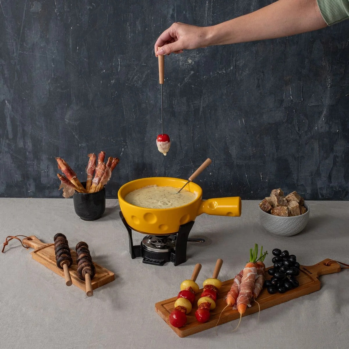 Boska Fondueset Super Cheesy in gebruik, hand dipt een vorkje met snacks eromheen