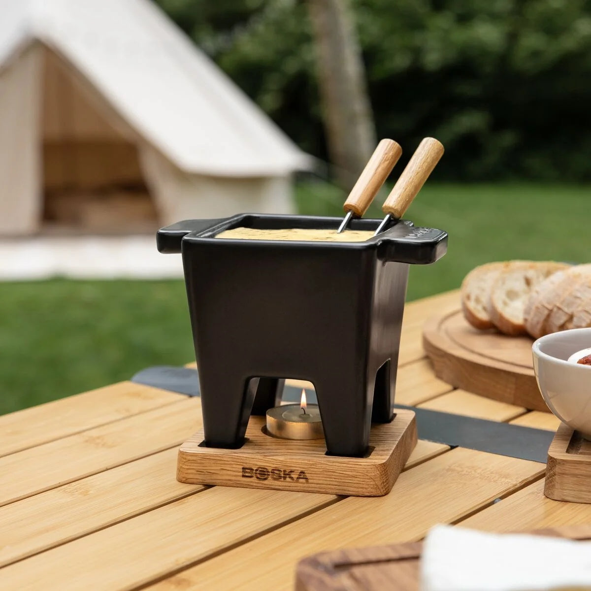 Boska Tapas Fondue Nero gevuld met kaasfondue buiten op een picknicktafel bij een tent
