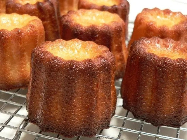 Gebakken canelés met donkere gekaramelliseerde korst en zachte binnenkant op een koelrooster