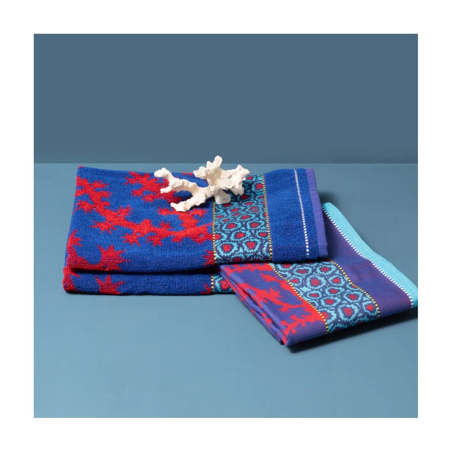 Mariëtte Wolbert Theedoek Koraal Blauw, gevouwen met een stuk koraal als decoratie erop, andere hoek