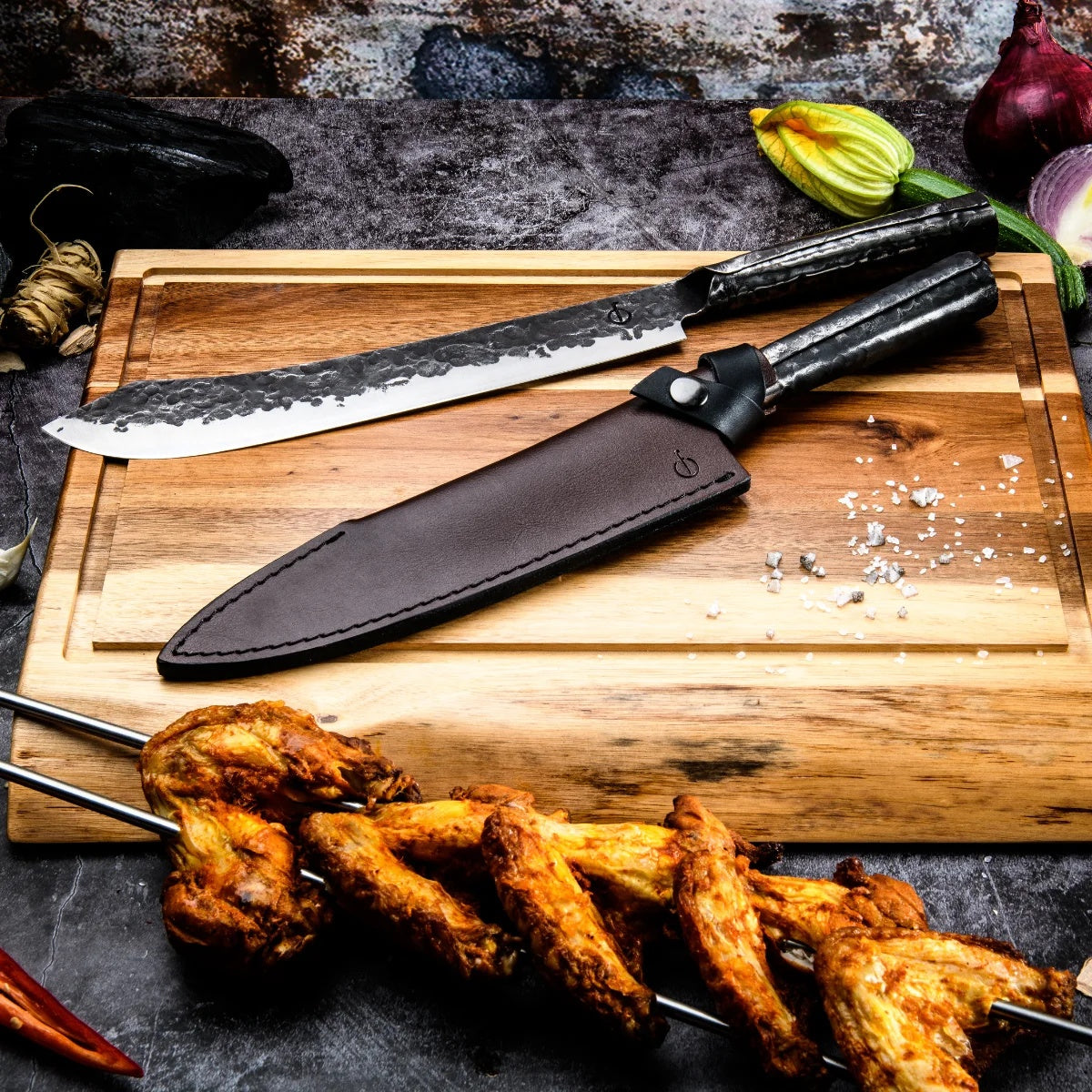 Koksmes met leren hoes op een houten snijplank tussen gegrilde kipspiesjes en groenten