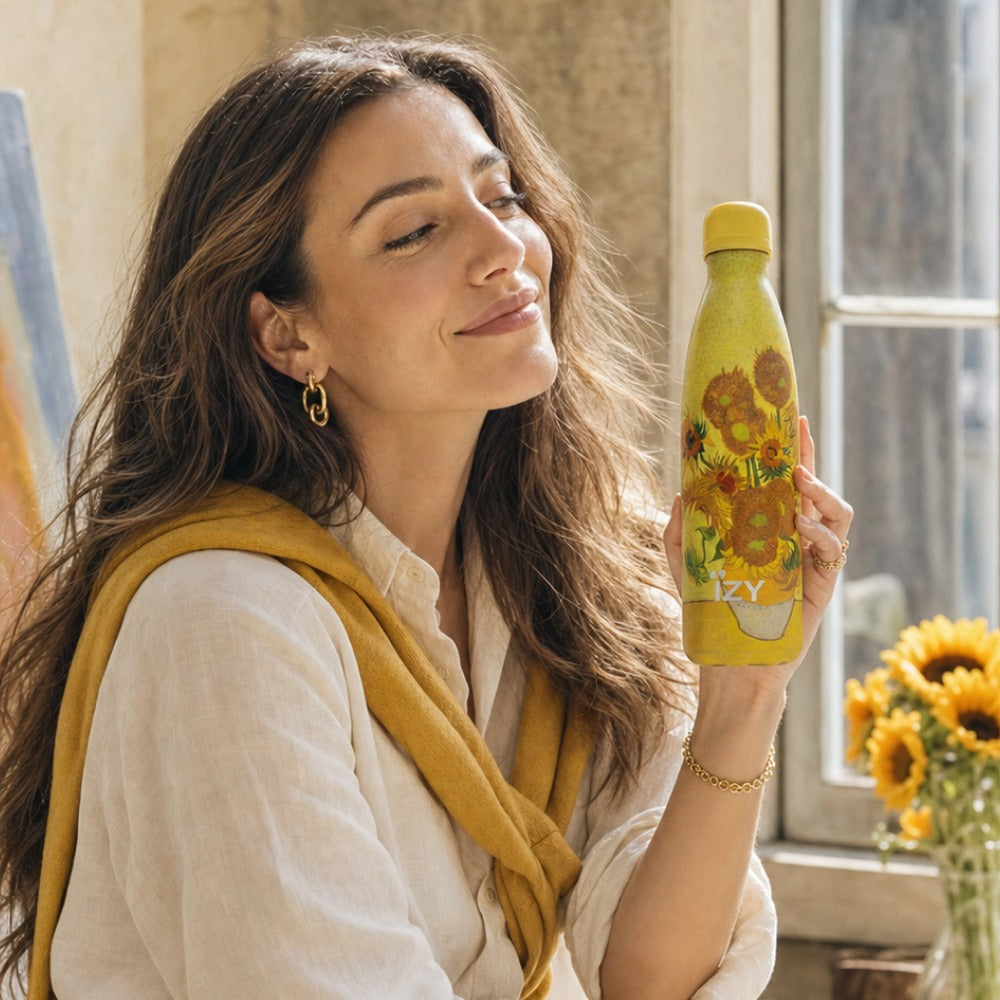 Vrouw houdt de gele IZY-thermosfles met Zonnebloemen van Van Gogh vast bij een raam met zonnebloemen