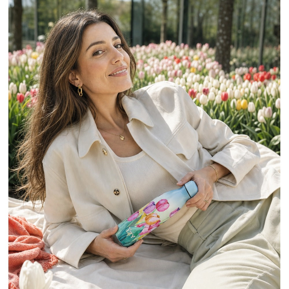 Vrouw zit tussen een bloeiend tulpenveld en houdt de IZY-thermosfles met aquarel tulpenmotief vast