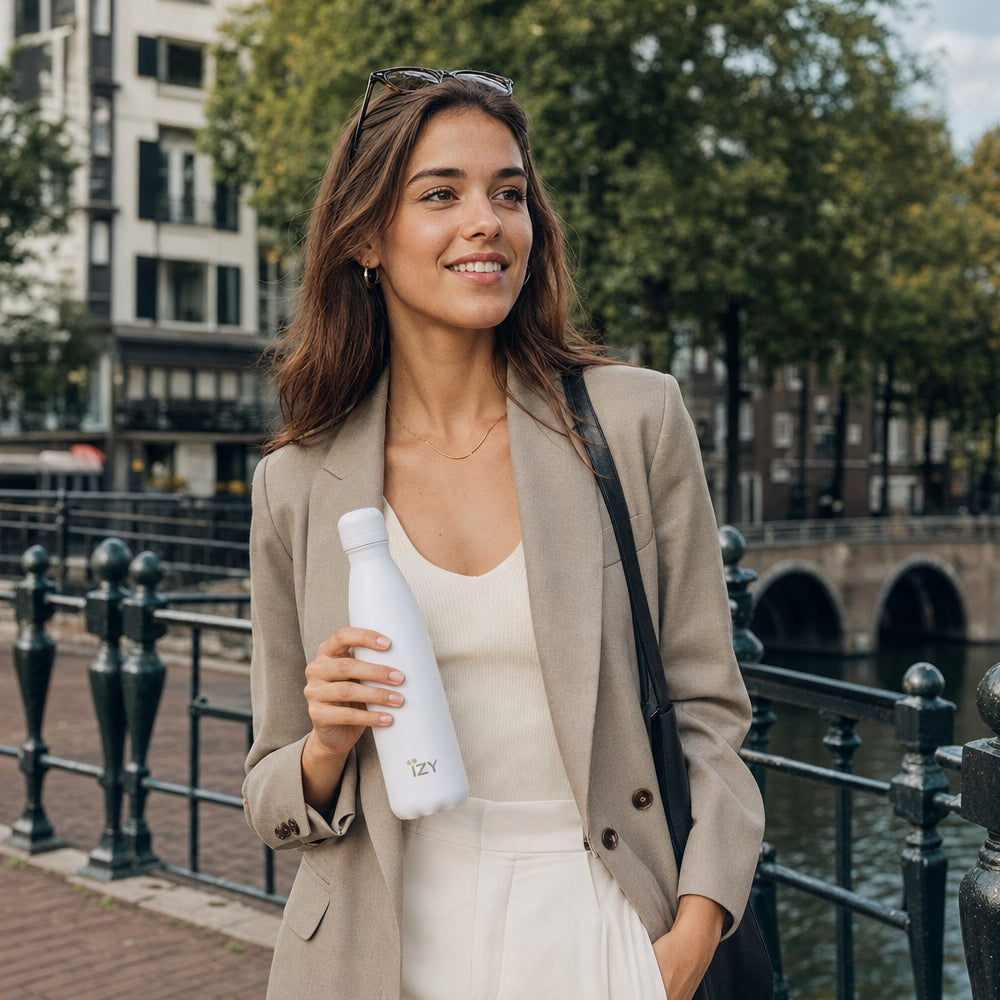 Vrouw in beige jas houdt de witte IZY Thermosfles vast bij een gracht