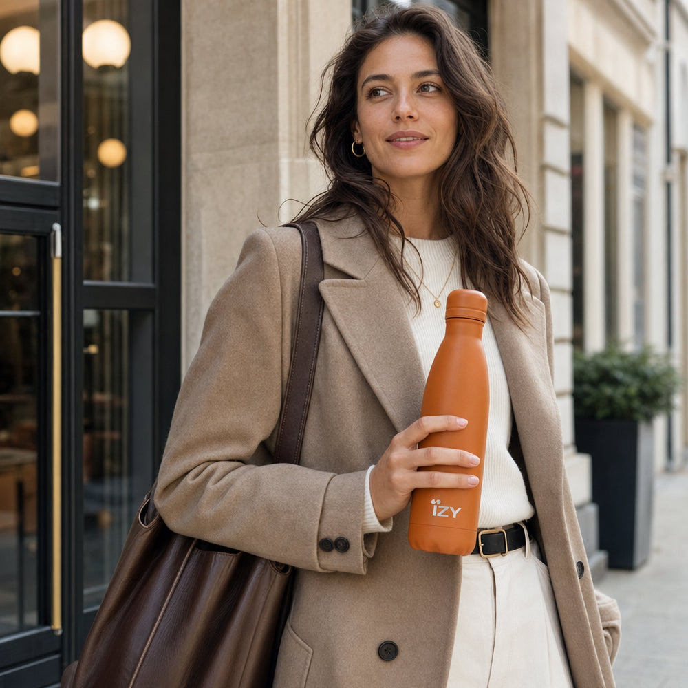 Vrouw in trenchcoat houdt de oranje IZY Thermosfles vast op straat