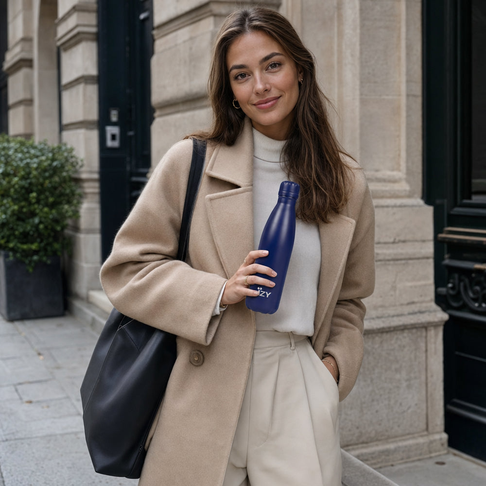 Vrouw in jas houdt de blauwe IZY Thermosfles vast voor een winkelpui