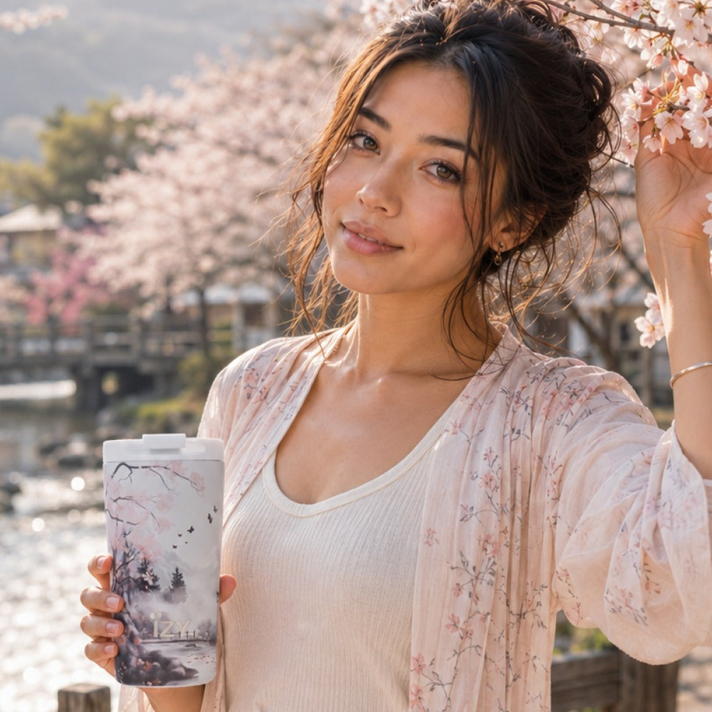 Vrouw houdt de IZY Thermosbeker Sakura Dreams vast onder een kersenbloesemboom