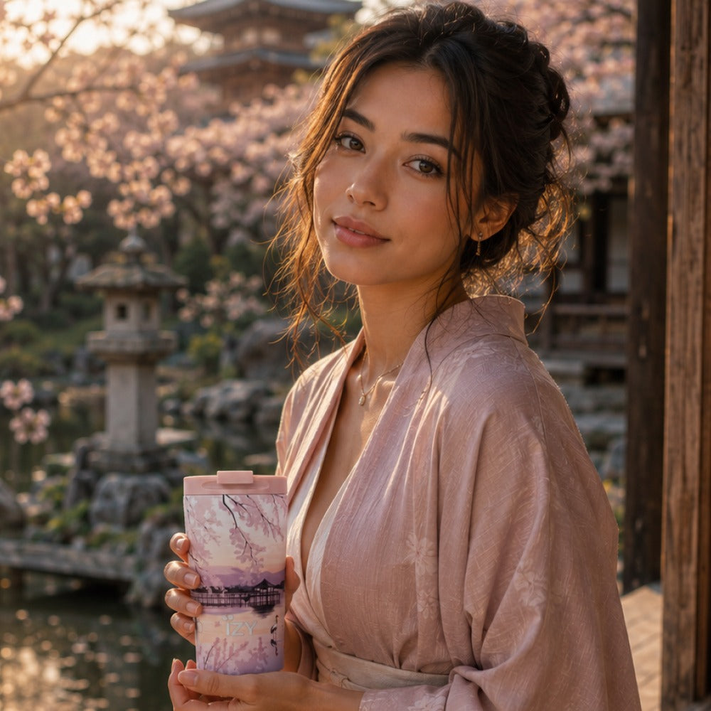 Vrouw in kimono houdt de IZY Thermosbeker Sunset Lake vast bij een Japanse tuin tijdens zonsondergang