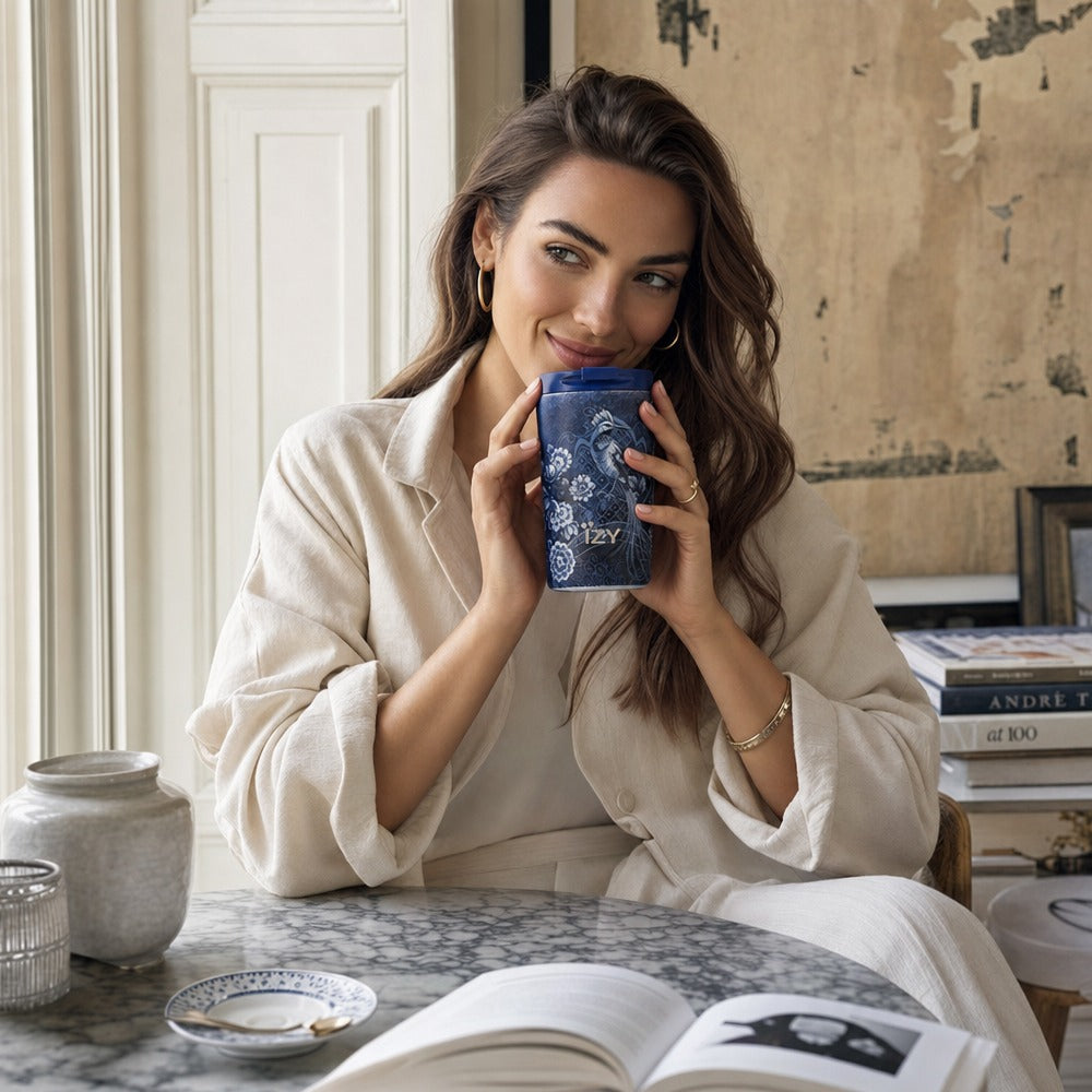 Vrouw aan tafel drinkt uit de IZY Thermosbeker Royal Blue met wit vogelmotief