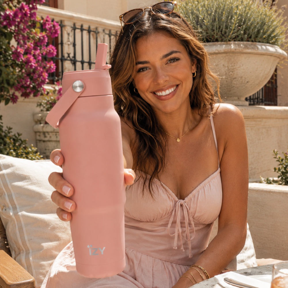 Vrouw houdt de zalmroze IZY Travel Bottle Salmon vast op een terras