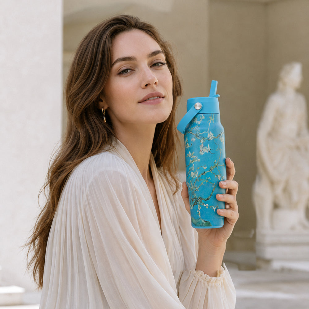 Vrouw bij een klassiek standbeeld houdt de IZY Travel Bottle Almond Blossom vast