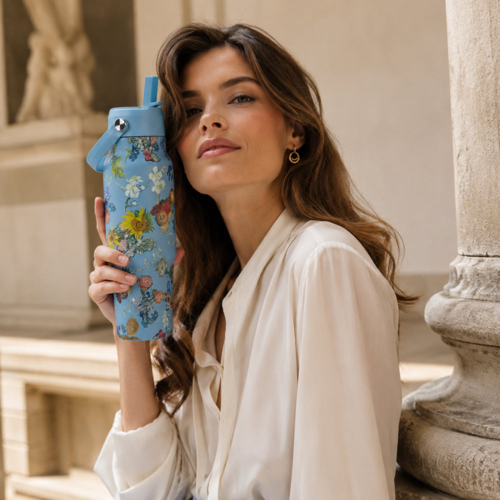 Vrouw in het wit houdt de IZY Travel Bottle Vincent's Flowers vast bij een standbeeld