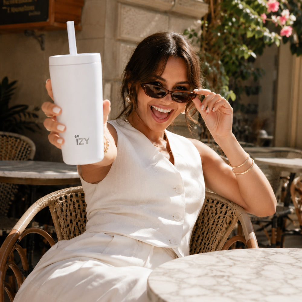 Vrouw met zonnebril houdt de witte IZY Tumbler met rietje vast op een terras