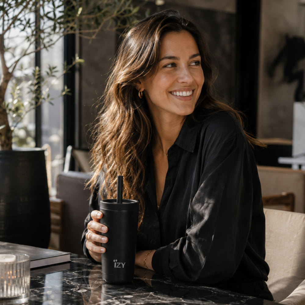 Vrouw in het zwart houdt de zwarte IZY Tumbler met rietje vast