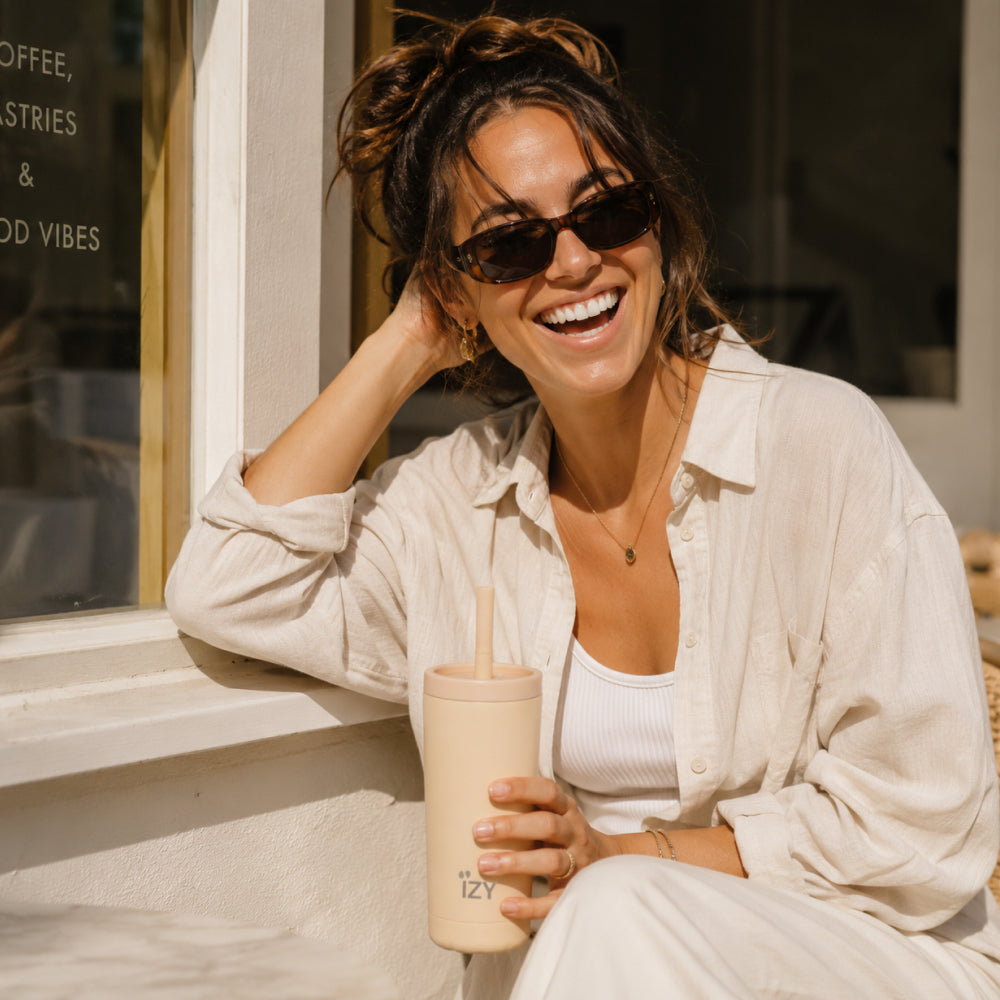 Vrouw lacht bij een raam en houdt de perzikkleurige IZY Tumbler Peach vast