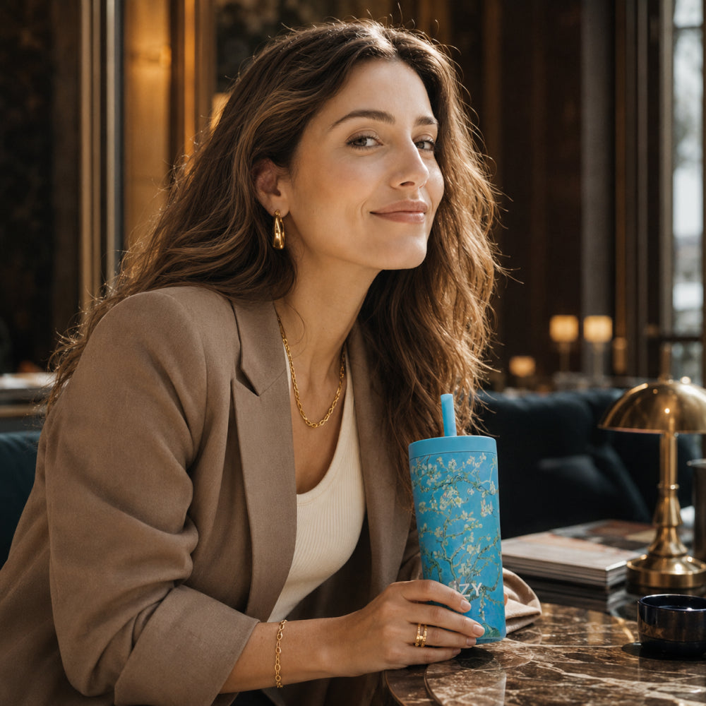 Vrouw in een gezellig interieur houdt de IZY Tumbler Almond Blossom met rietje vast
