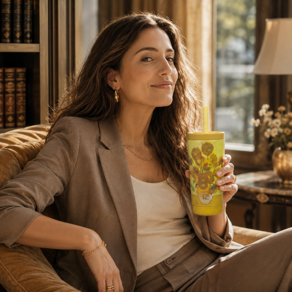 Vrouw in een fauteuil houdt de gele IZY Tumbler Sunflowers met rietje vast