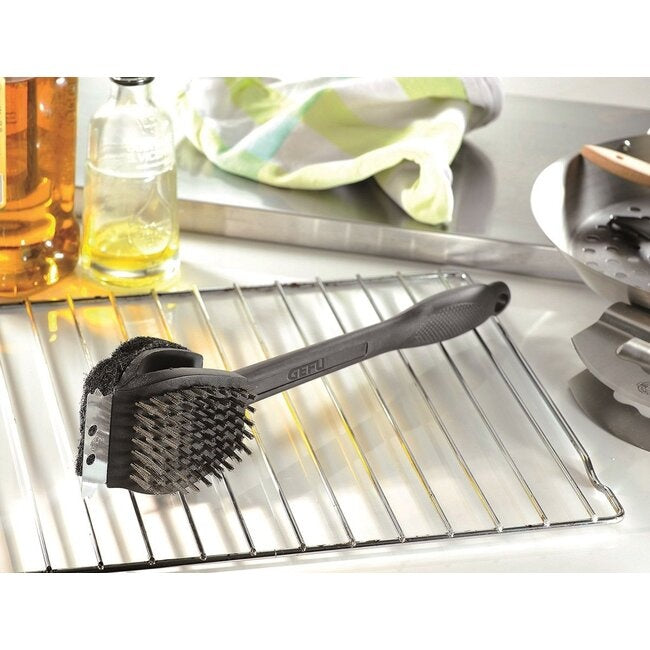 GEFU Barbecueborstel 3-in-1 liggend op een barbecuerooster naast een oliefles, doek en ander bbq-gereedschap