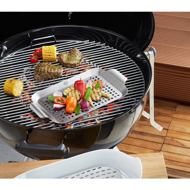 GEFU Grillpan - Klein, gevuld met gegrilde groente op het rooster van een kogelbarbecue, met een houten tafel en snijplank op de achtergrond