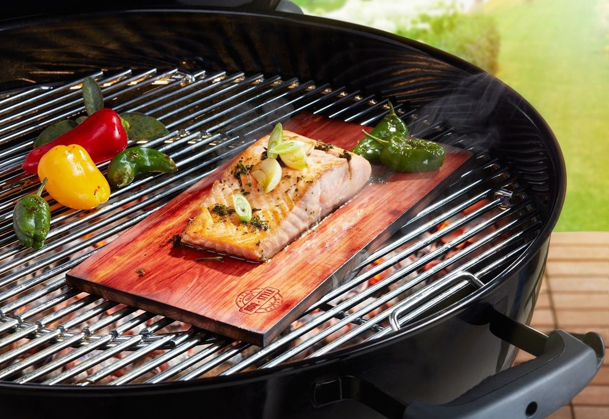GEFU Cederhouten Grillplanken - 2 stuks, geschroeide plank op een barbecuerooster met een stuk gegrilde zalm en paprika's erop