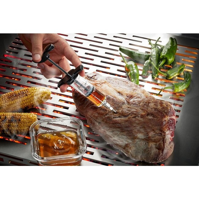 GEFU Marinadespuit, close-up van een hand die marinade in een stuk vlees op de barbecue spuit, met maiskolven, groene pepers en een bakje marinade ernaast