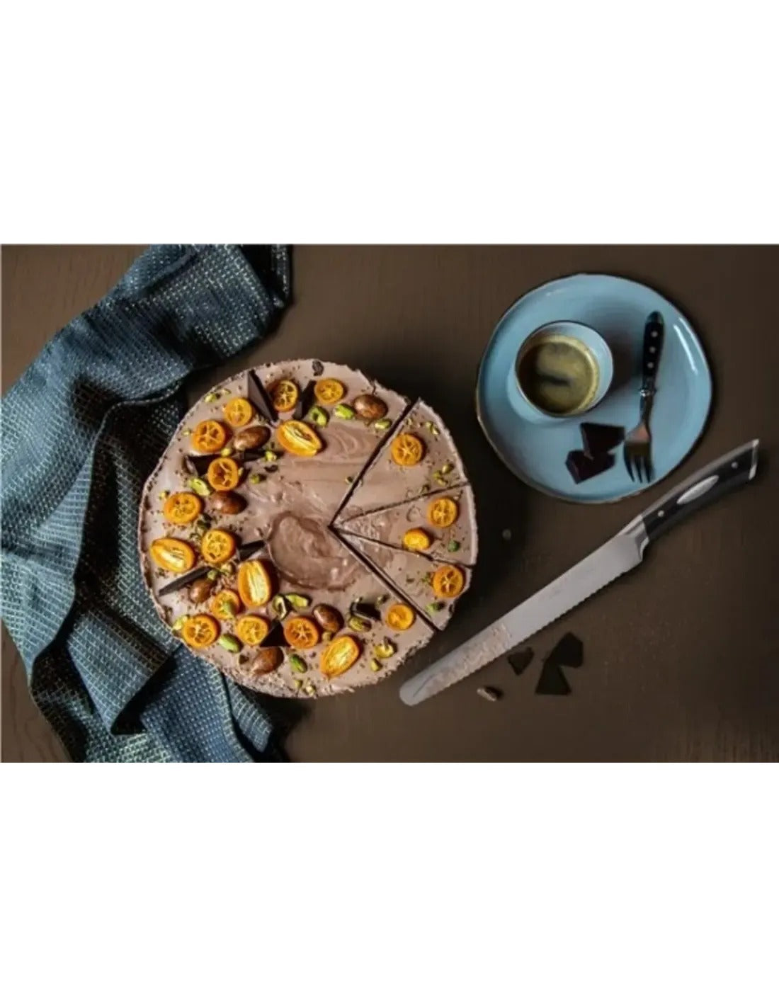 Scanpan Classic Broodmes ligt op een donkere tafel naast een aangesneden chocoladetaart met kumquats, een kopje koffie en een vorkje op een blauw bord