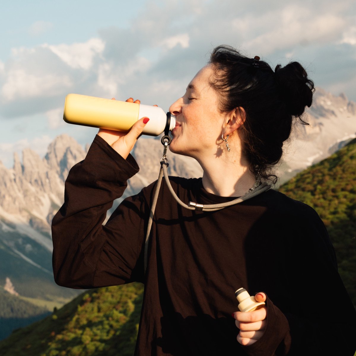 Vrouw drinkt rechtstreeks uit de Dopper Insulated Maple Yellow met bergtoppen op de achtergrond