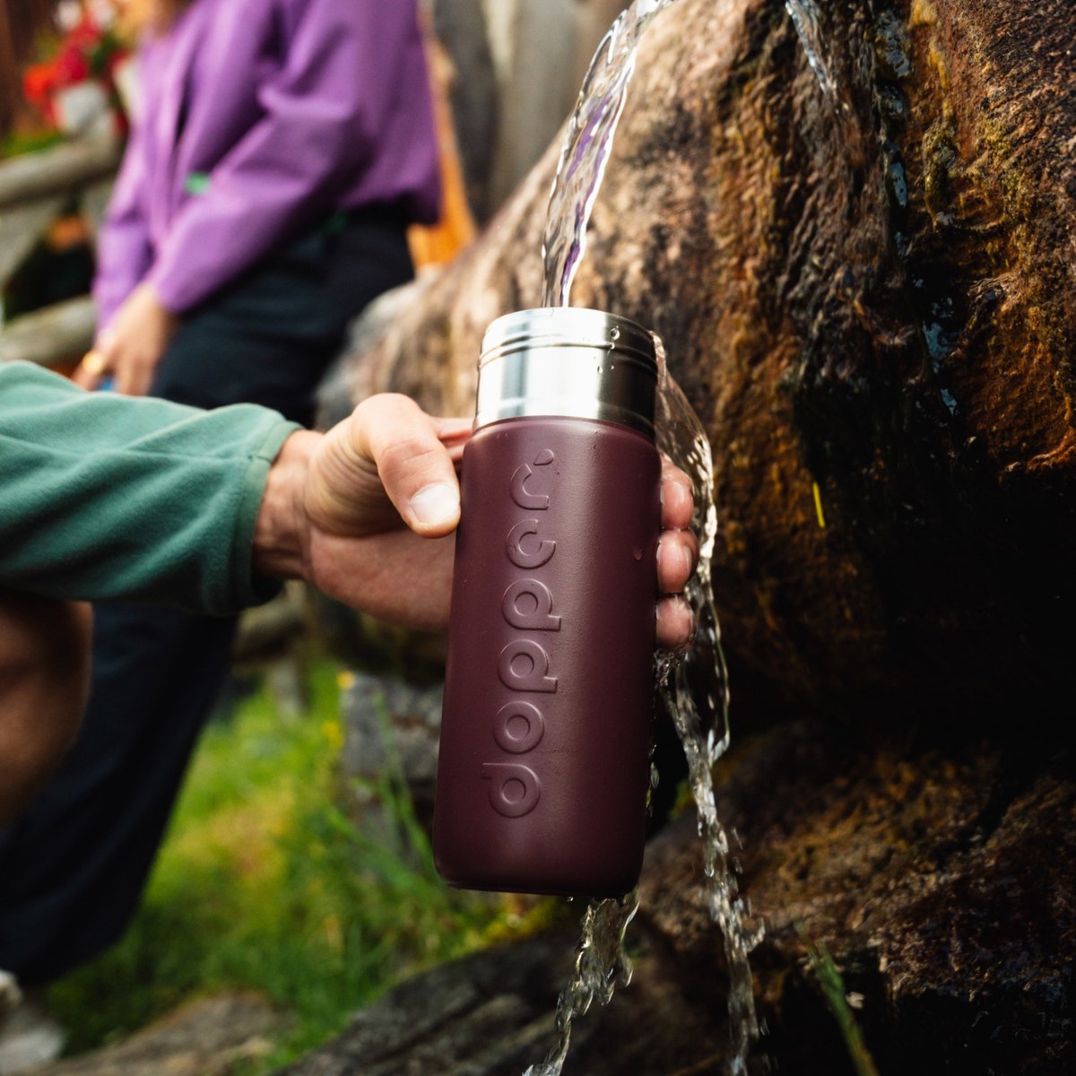 Hand vult de Dopper Insulated Cedar Brown met vers bronwater bij een waterval