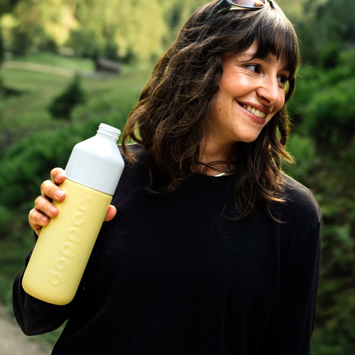 Lachende vrouw houdt de Dopper Insulated Maple Yellow vast in een groene buitenomgeving