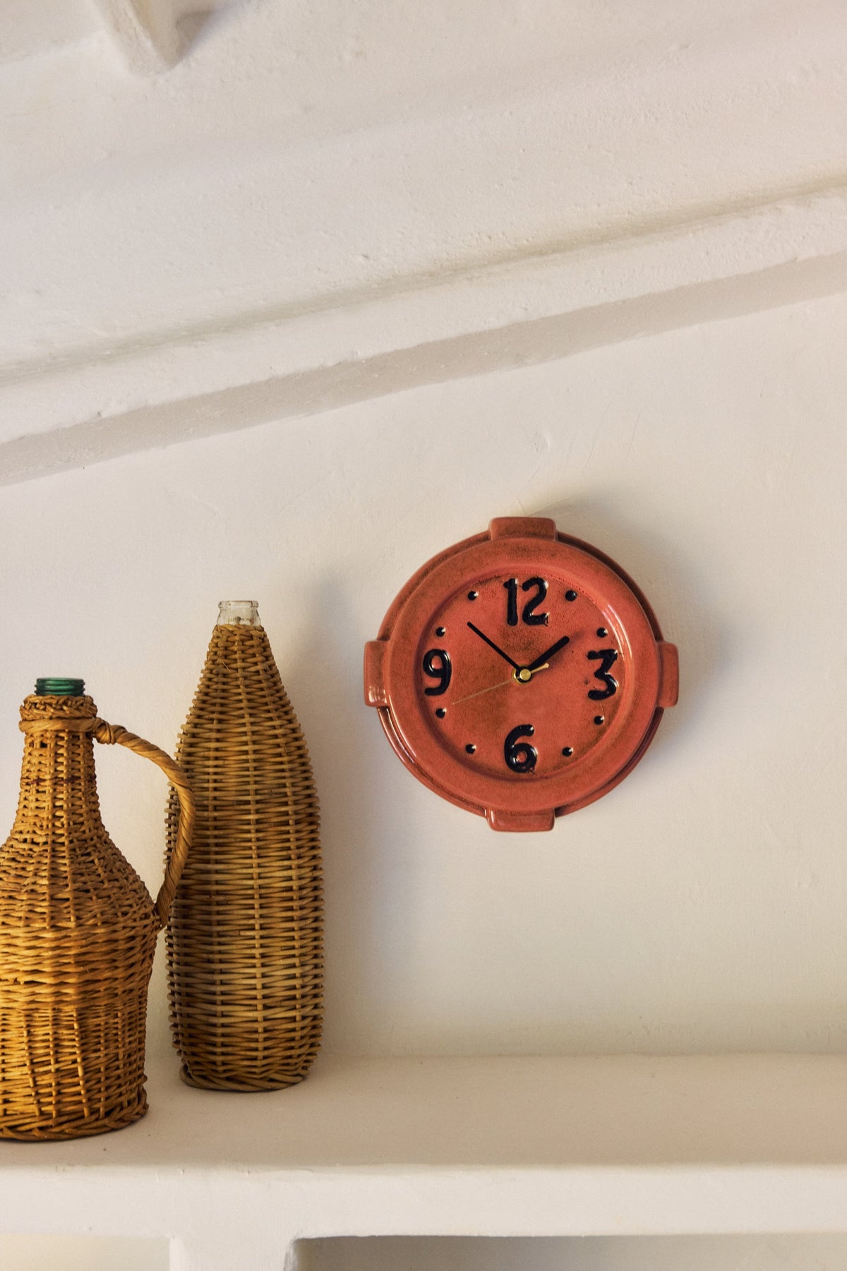 HKLiving 70's Wandklok Pink aan de wand naast aardewerken potten